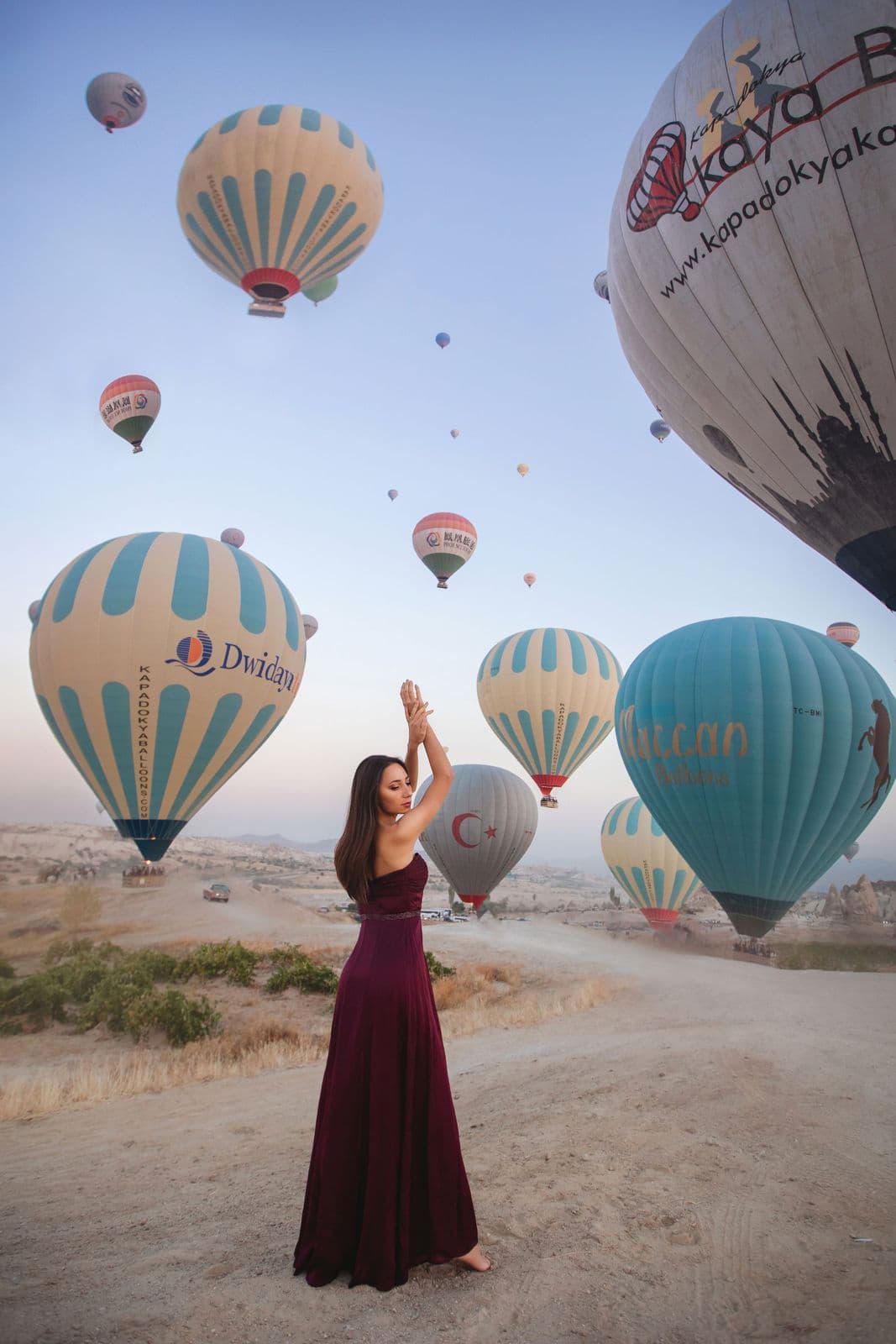 A woman in a red dress posing with hot air balloons at sunrise in Cappadocia