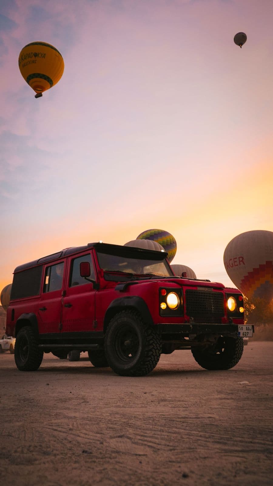 A red jeep parked under hot air balloons at sunrise in Cappadocia
